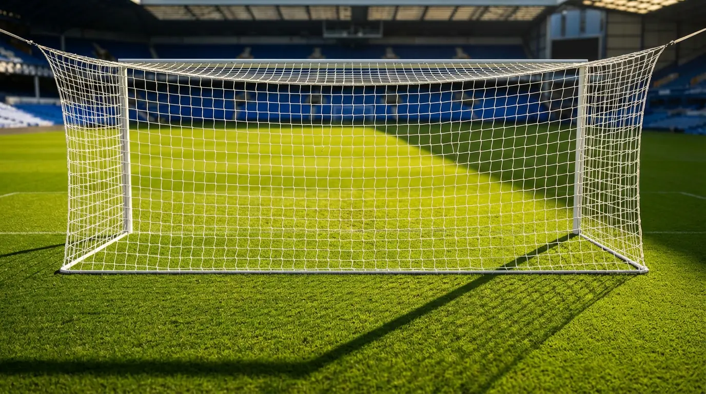 Fussballtor mit weissem Netz im Sonnenlicht auf einem professionellen Spielfeld